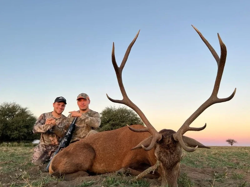 Two hunters posing with a Spanish red deer